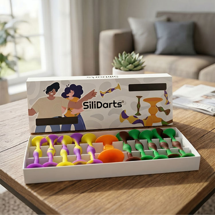 Offene Verpackung eines bunten Wurfspiels mit Saugnapf-Darts in verschiedenen Farben auf einem Holztisch im Wohnzimmer.